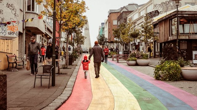 Een volwassene en een kind wandelen hand in hand over een straat beschilderd in regenboogkleuren.